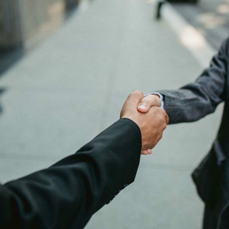Close-up of two businessmen shaking hands outside, symbolizing partnership and agreement.