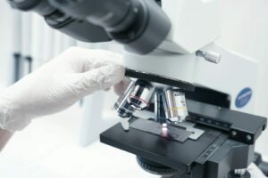 A person in white gloves looking through a microscope