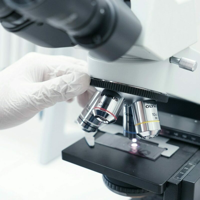 A person in white gloves looking through a microscope