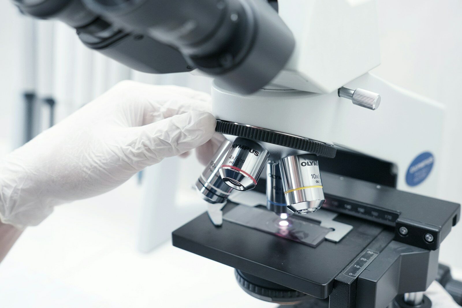 A person in white gloves looking through a microscope