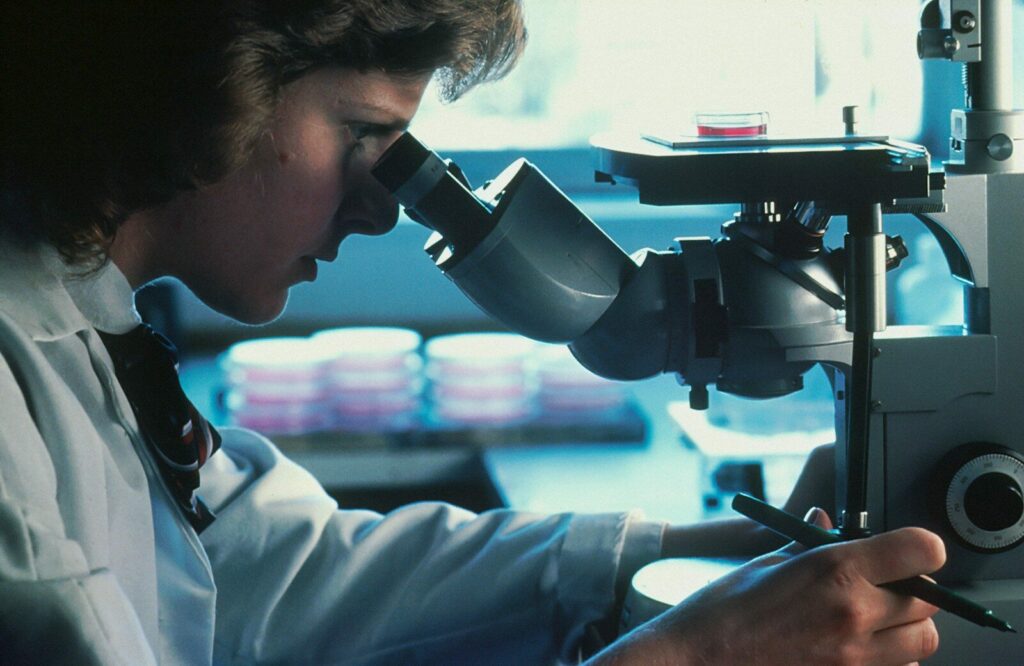 A person in a white lab coat looking through a microscope in a laboratory