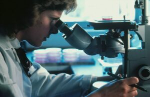 A person in a white lab coat looking through a microscope in a laboratory