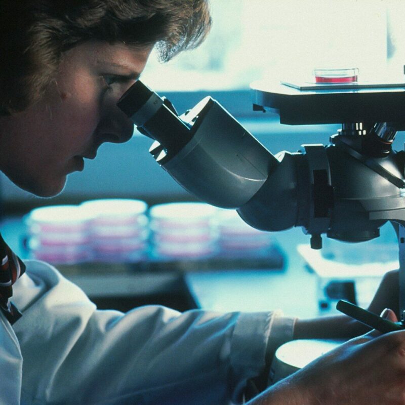 A person in a white lab coat looking through a microscope in a laboratory